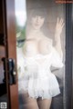 A woman in a white dress standing in front of a window.