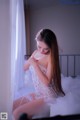 A woman in a white lingerie sitting on a bed.