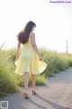 A woman in a yellow dress walking down a dirt road.