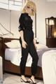 A woman in a black jumpsuit standing in front of a bed.