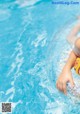 A little girl in a yellow bikini playing in a pool.