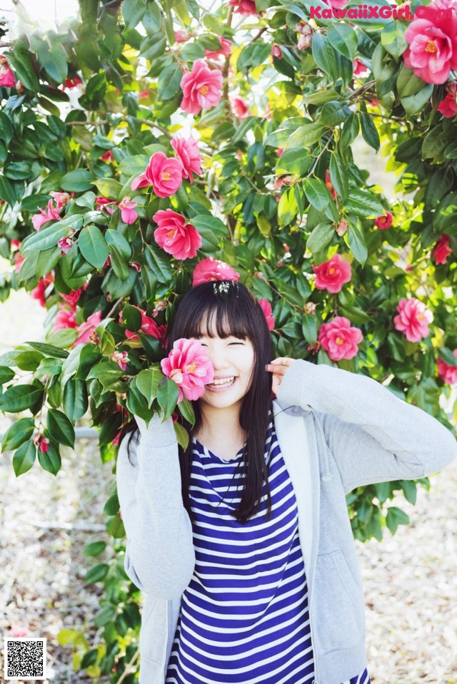 A woman standing in front of a bush of pink flowers.